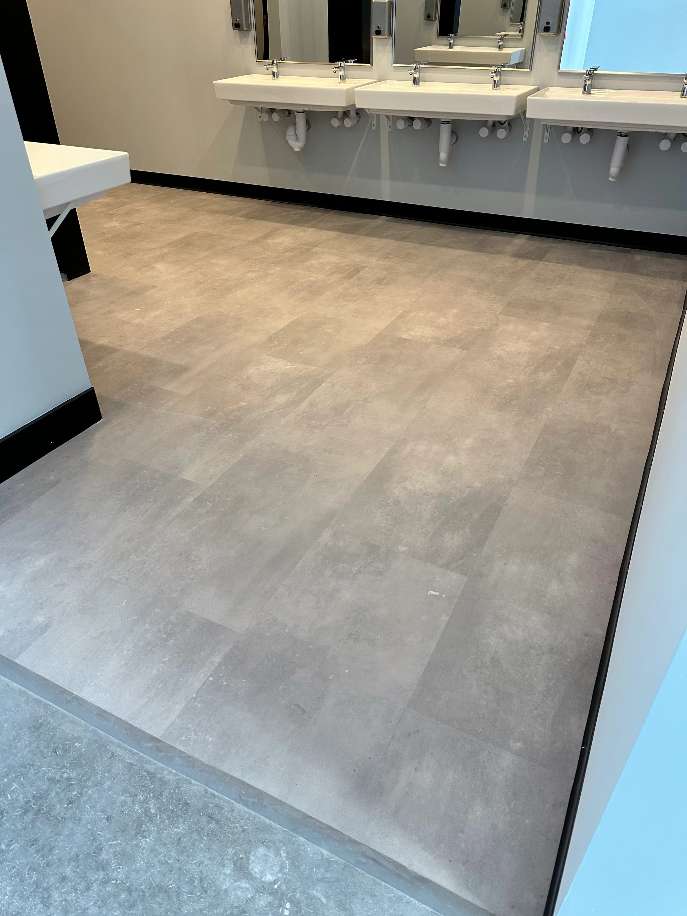 Row of three wall-mounted white sinks above HRK Titanium tile flooring in the multi-family public restroom